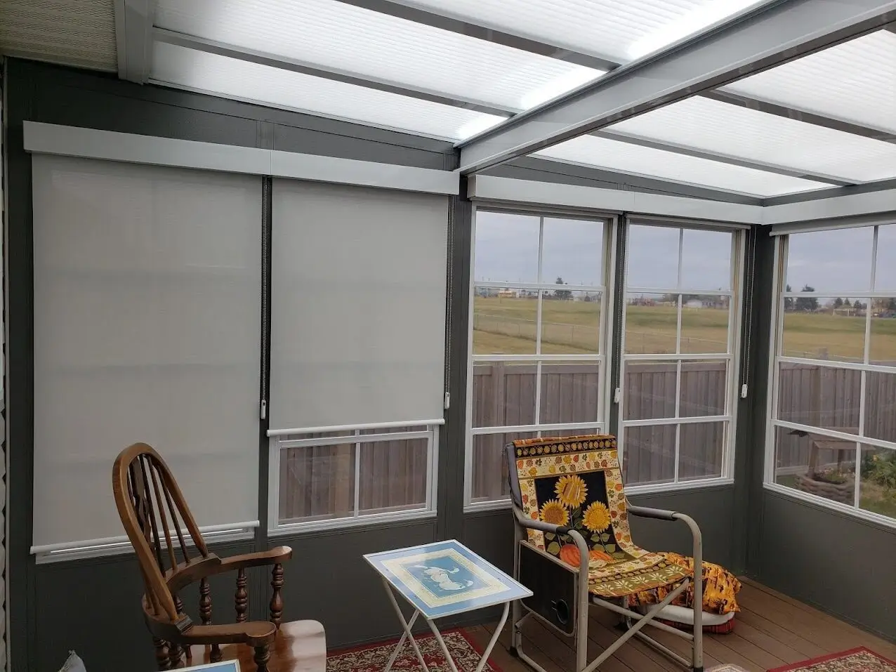 A Sunroom with a chair and table by a window, equipped with roll shutters for light control.