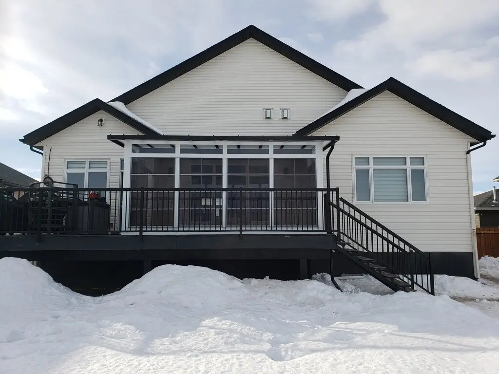 A house featuring a large deck, a balcony, and a Sunroom, surrounded by greenery.