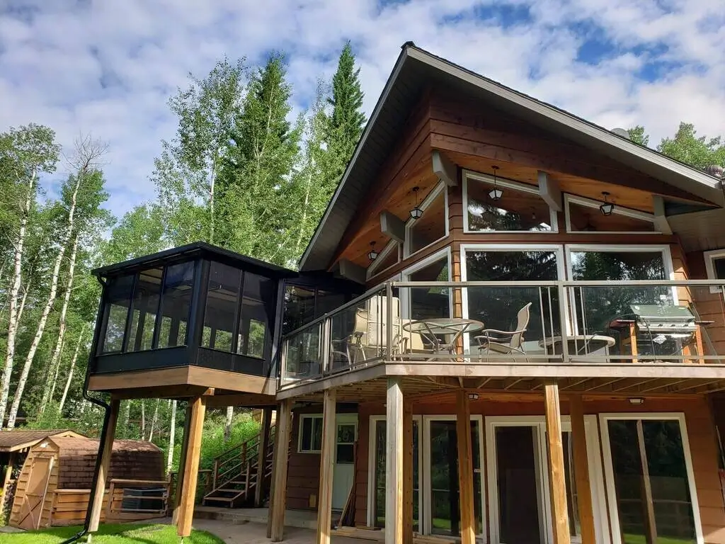A large home featuring a spacious deck and a balcony, surrounded by greenery.