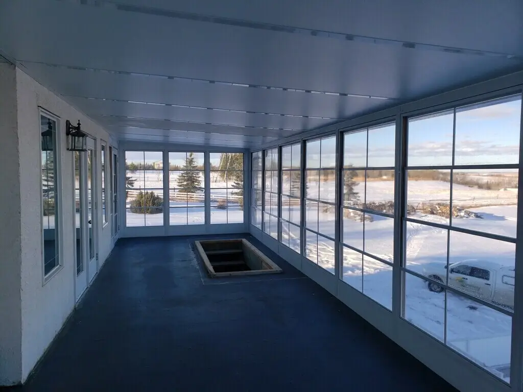 A sunroom featuring large windows overlooks a spacious pool, complemented by stylish patio covers.