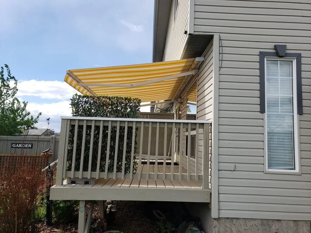 A bright yellow Retractable Awning extends over a wooden deck, providing shade and a cheerful outdoor atmosphere.