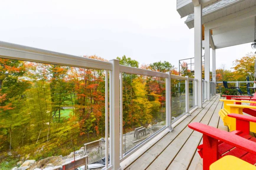 A deck featuring colorful chairs and a glass aluminum railing, overlooking a lush green forest.