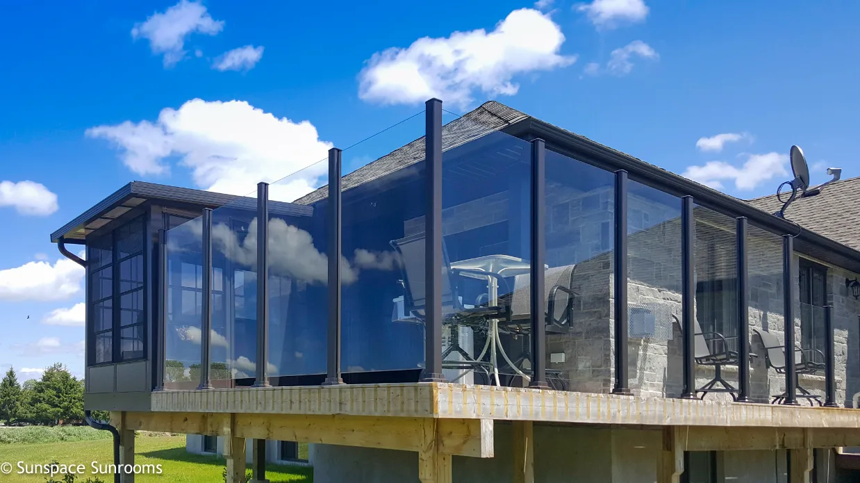 A stylish glass-enclosed porch with a deck and patio, complemented by a topless glass railing for a modern look.
