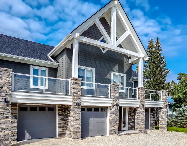 A residence with stone walls, a garage, and elegant aluminum railing complemented by glass.