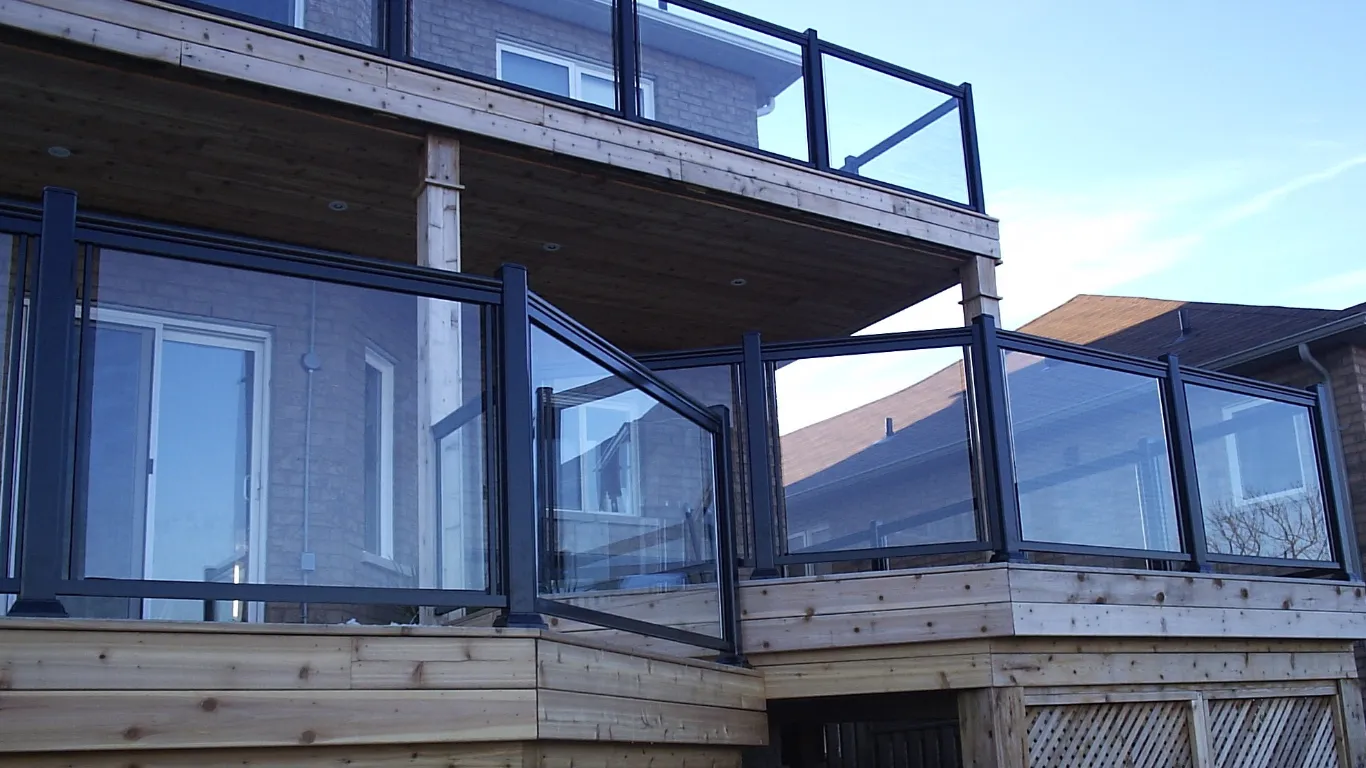 A contemporary wooden deck with a glass railing, showcasing a stylish aluminum frame for a clear view.